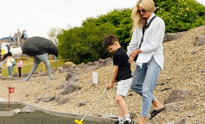 Dinosaur themed mini-golf with a mother and child playing golf